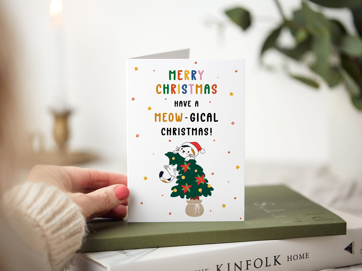 Christmas card which reads 'merry christmas have a meow-gical christmas' with a cartoon illustration of a cat jumping on a christmas tree.