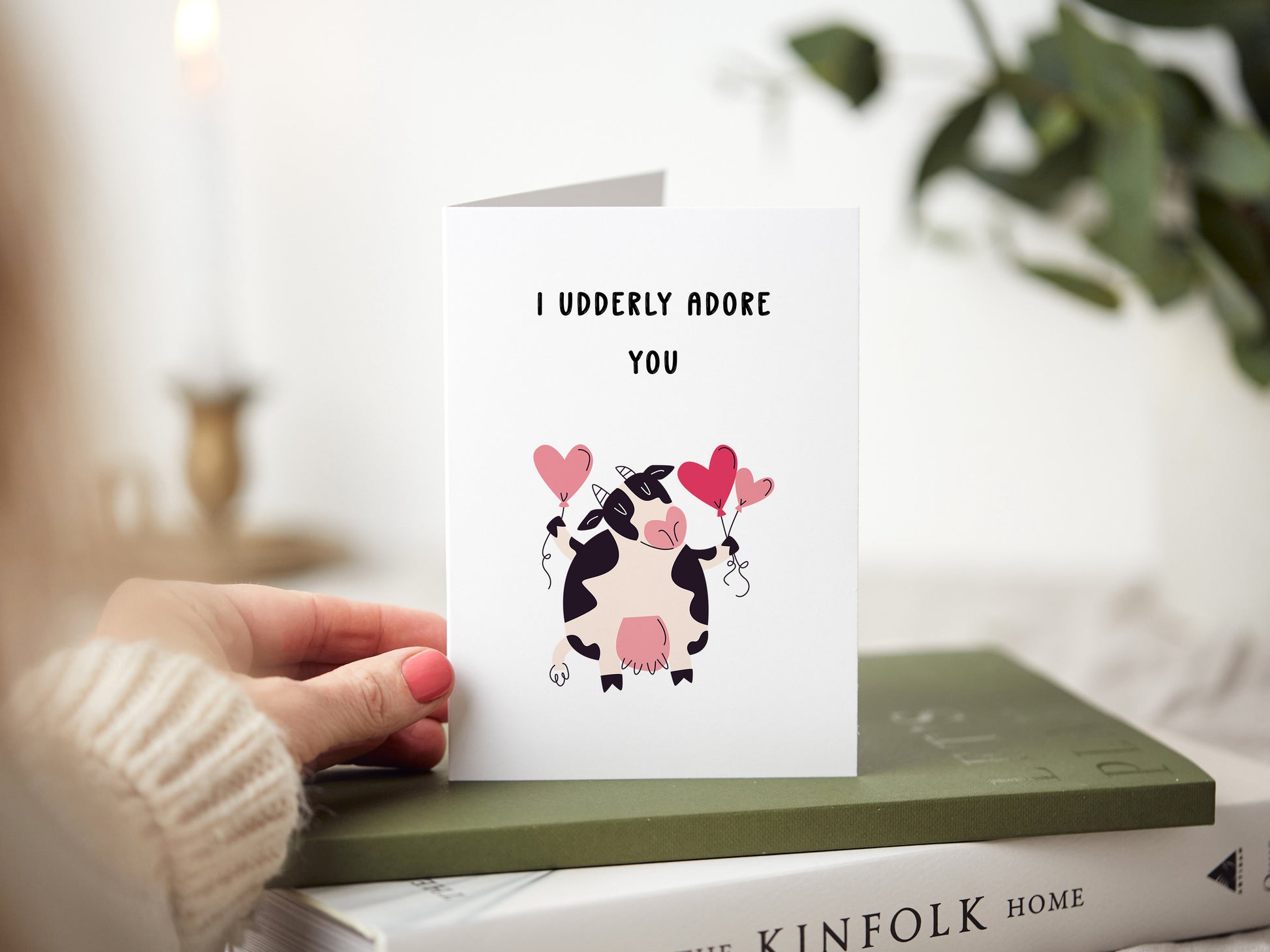 Anniversary card which reads 'I udderly adore you' with a illustration of a cow holding heart balloons.