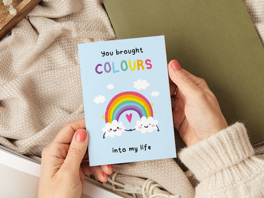 Greeting card which reads 'you brought colours into my life' with an illustration of two clouds holding hands and a rainbow.